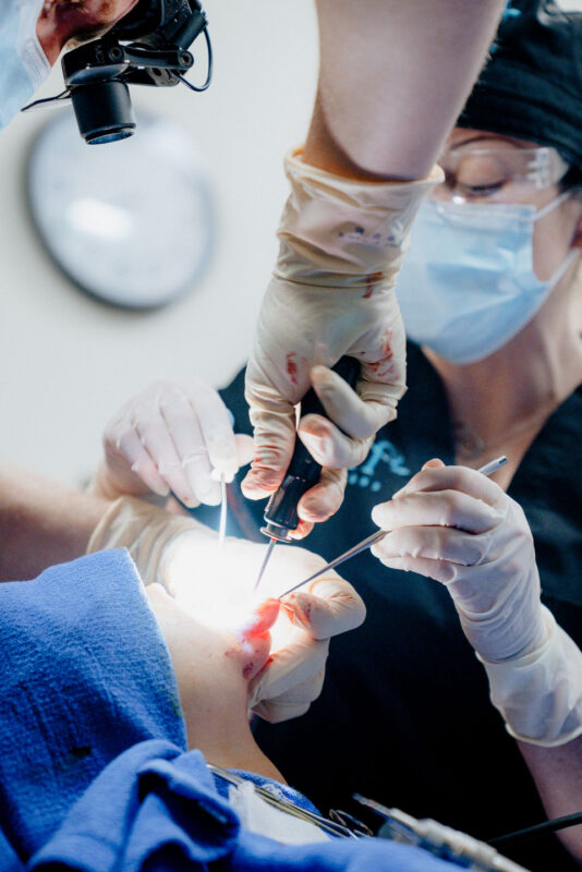 CMF surgical team performing oral or maxillofacial procedure with illuminated instruments, gloved hands, and sterile environment in a clinical operating room.