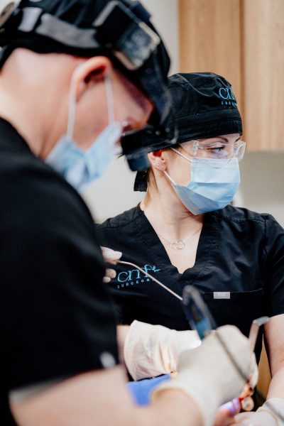 CMF surgeons performing a procedure in a sterile operating room, with Dr. Tim Osborn using magnification headset and surgical instruments.